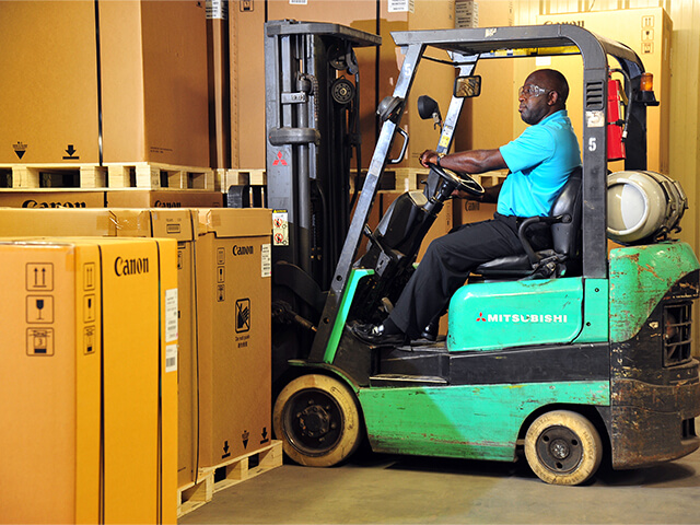 Man driving heavily used green forklift in warehouse
